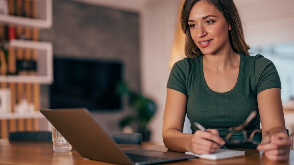 Woman taking notes and looking at a laptop