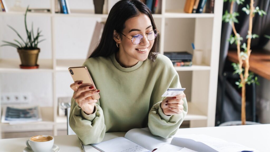 Girl smiling with phone in one hand and credit card in another