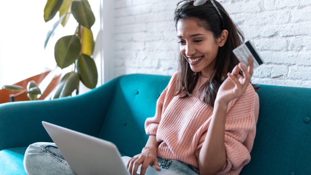 Woman on the couch using laptop and holding credit card