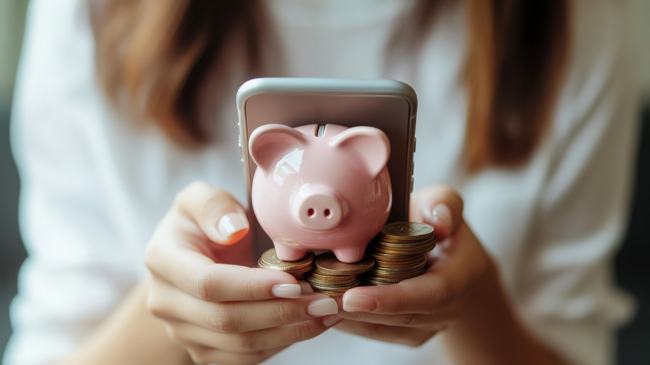 Woman holding phone and piggy bank