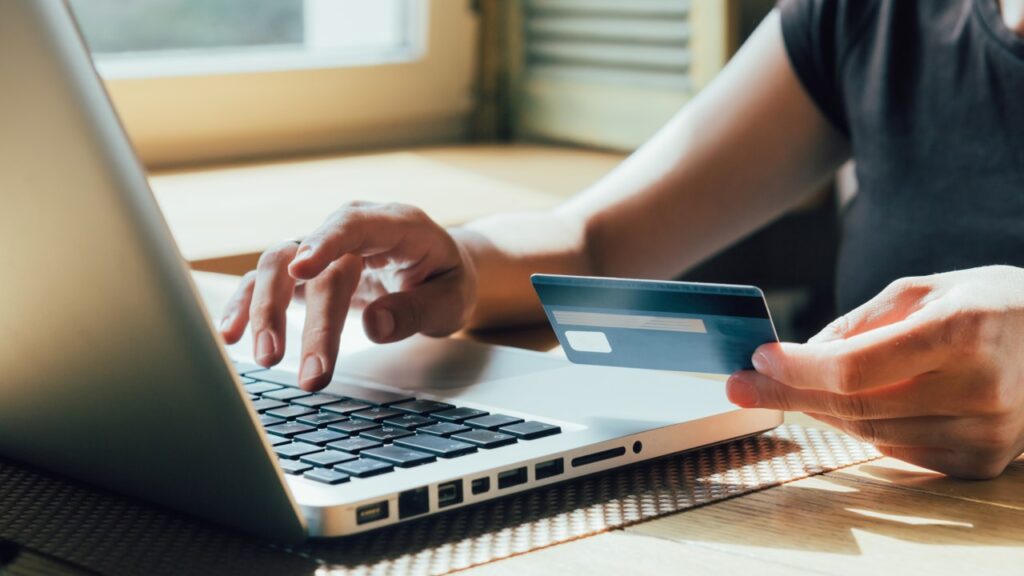 Hand holding card while typing on laptop